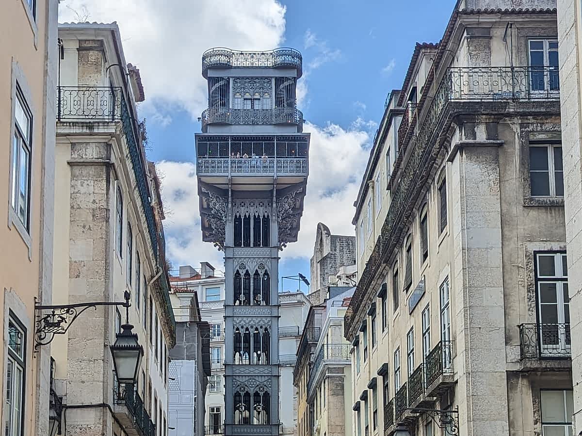 Der Elevador de Santa Justa, ein historischer, metallener Aufzugsturm im neugotischen Stil, eingefasst von traditionellen, mehrstöckigen Gebäuden in der Baixa, Lissabon.